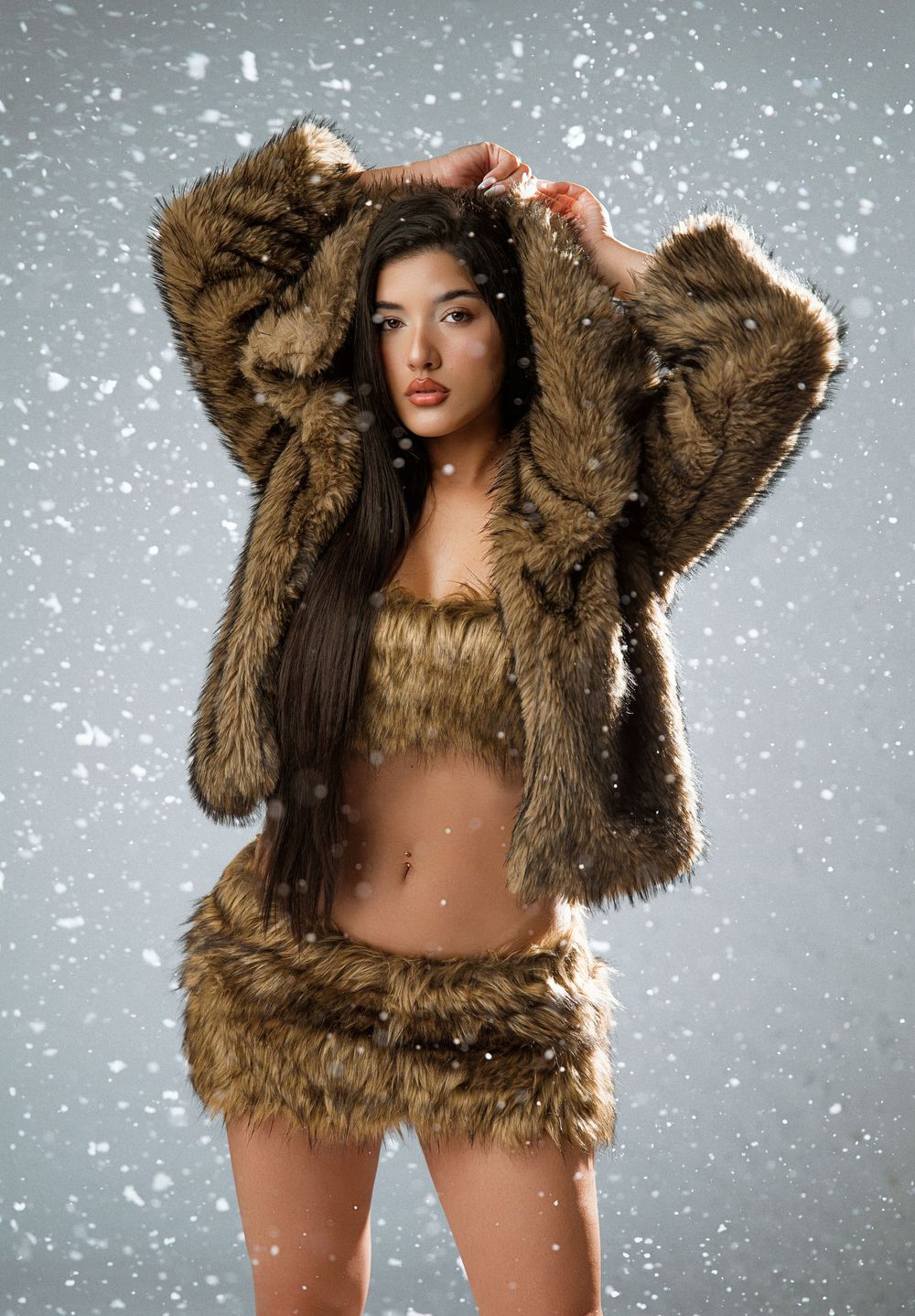 Woman in fur set with hooded jacket poses in snowy studio backdrop.