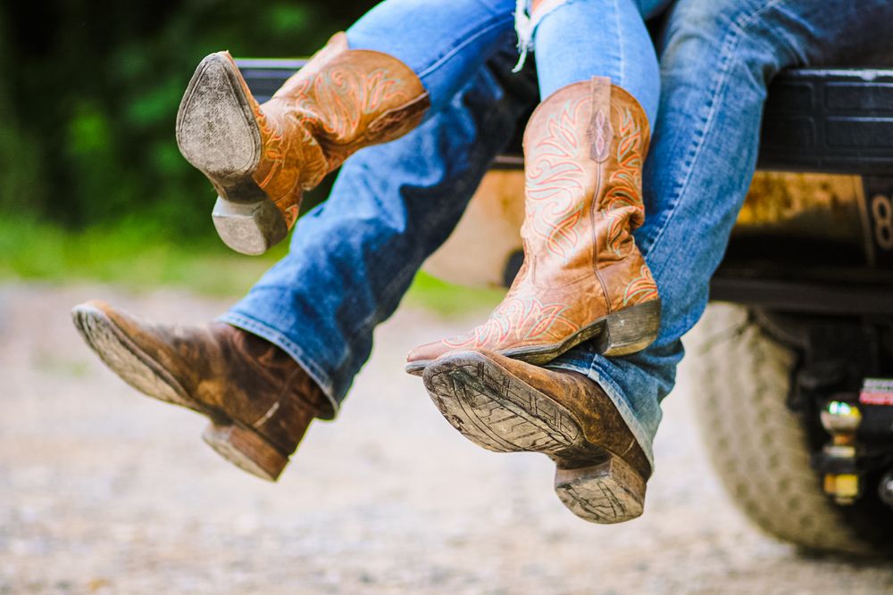 Lifestyle image showing Boots of a couple swinging back and forth while sitting on a tailgate of a truck.