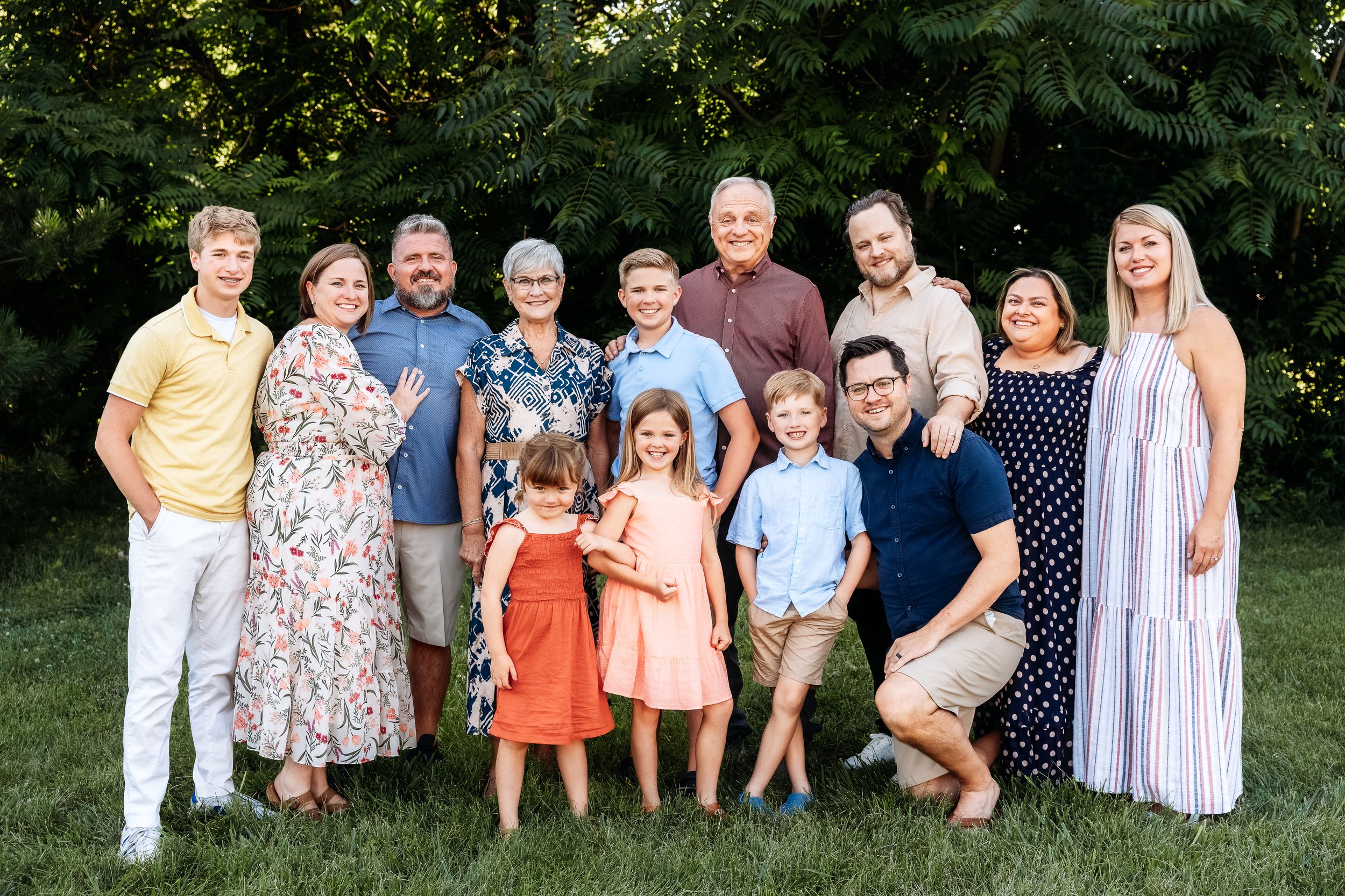 Group of people wearing coordinated summer outfits pose together outdoors in a garden setting during golden hour.