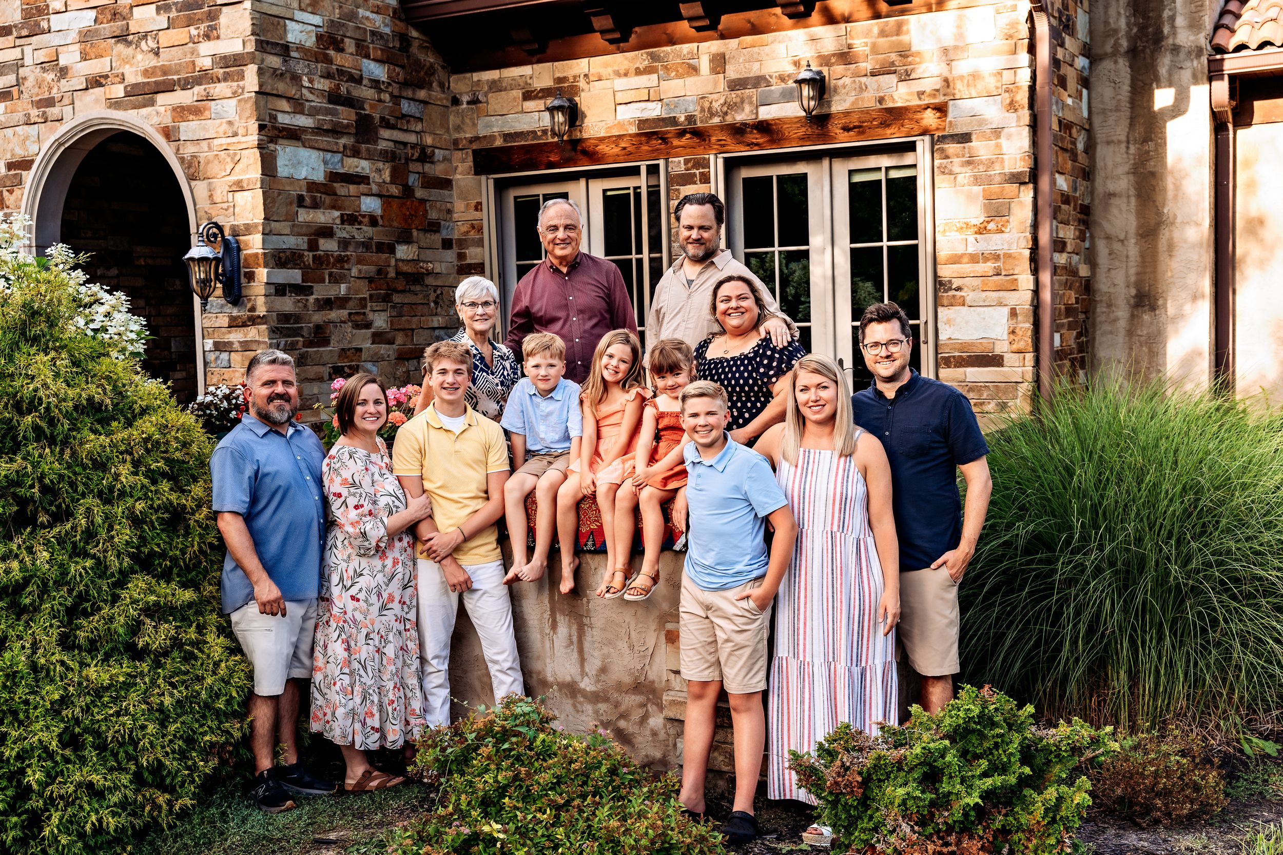 A group poses together against a rustic brick wall and garden setting for outdoor family portraits.
