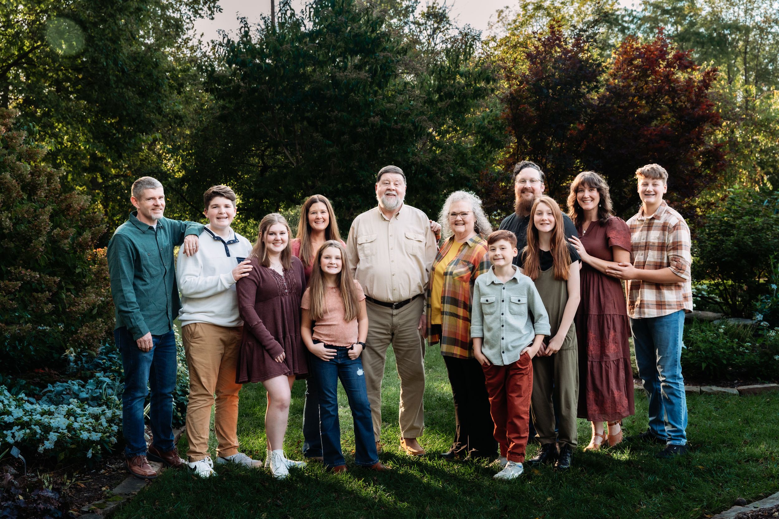 A group of people standing together outdoors in a garden setting during autumn wearing casual clothing.