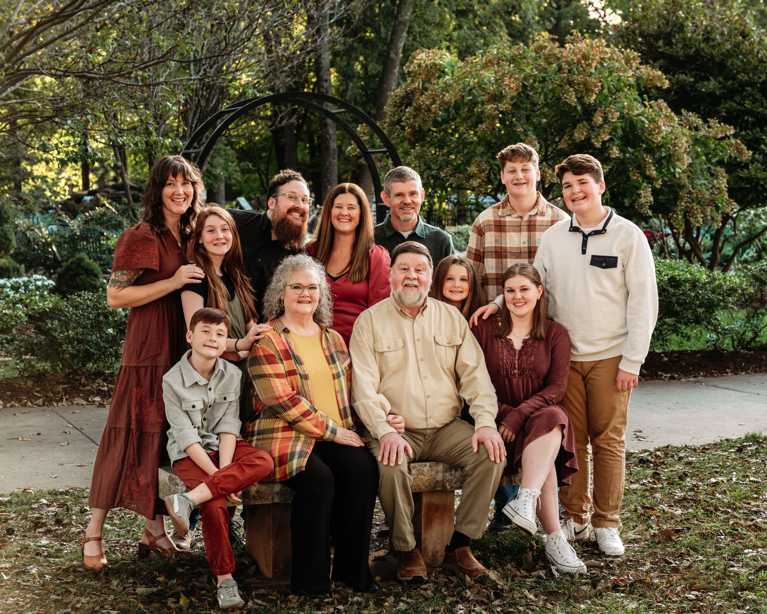 A series of outdoor family portraits taken in a park setting with people wearing warm autumn colors and casual attire.