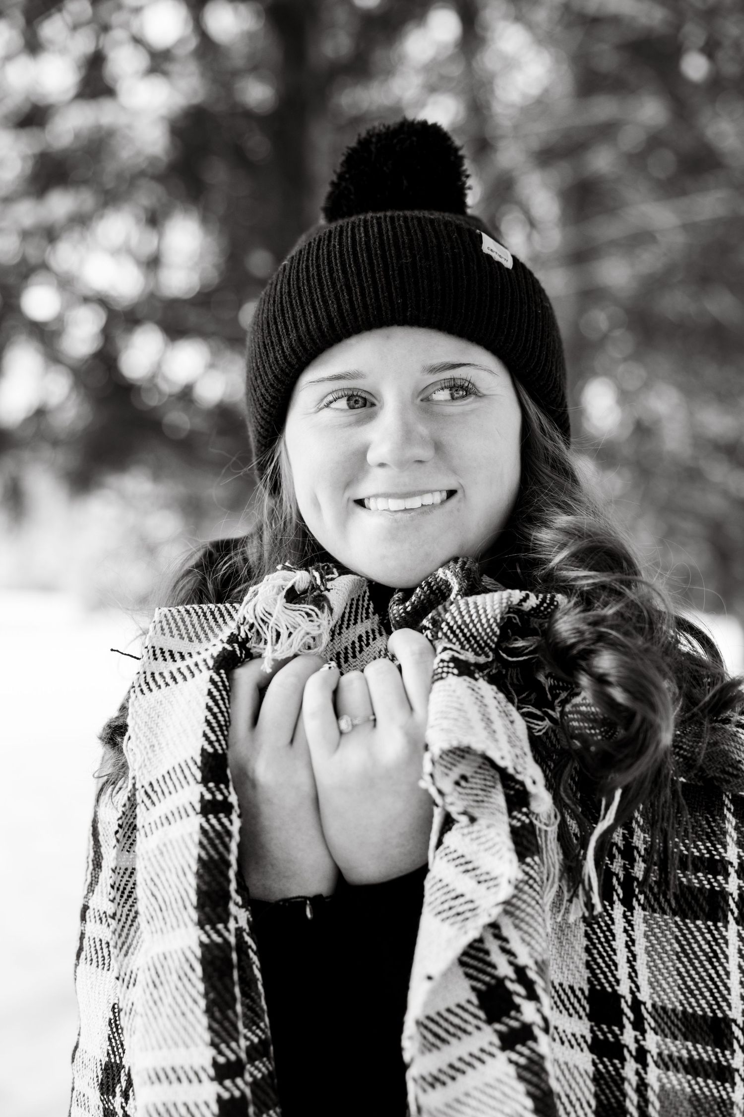 Winter portrait featuring plaid blanket and black knit hat against blurred snowy background.