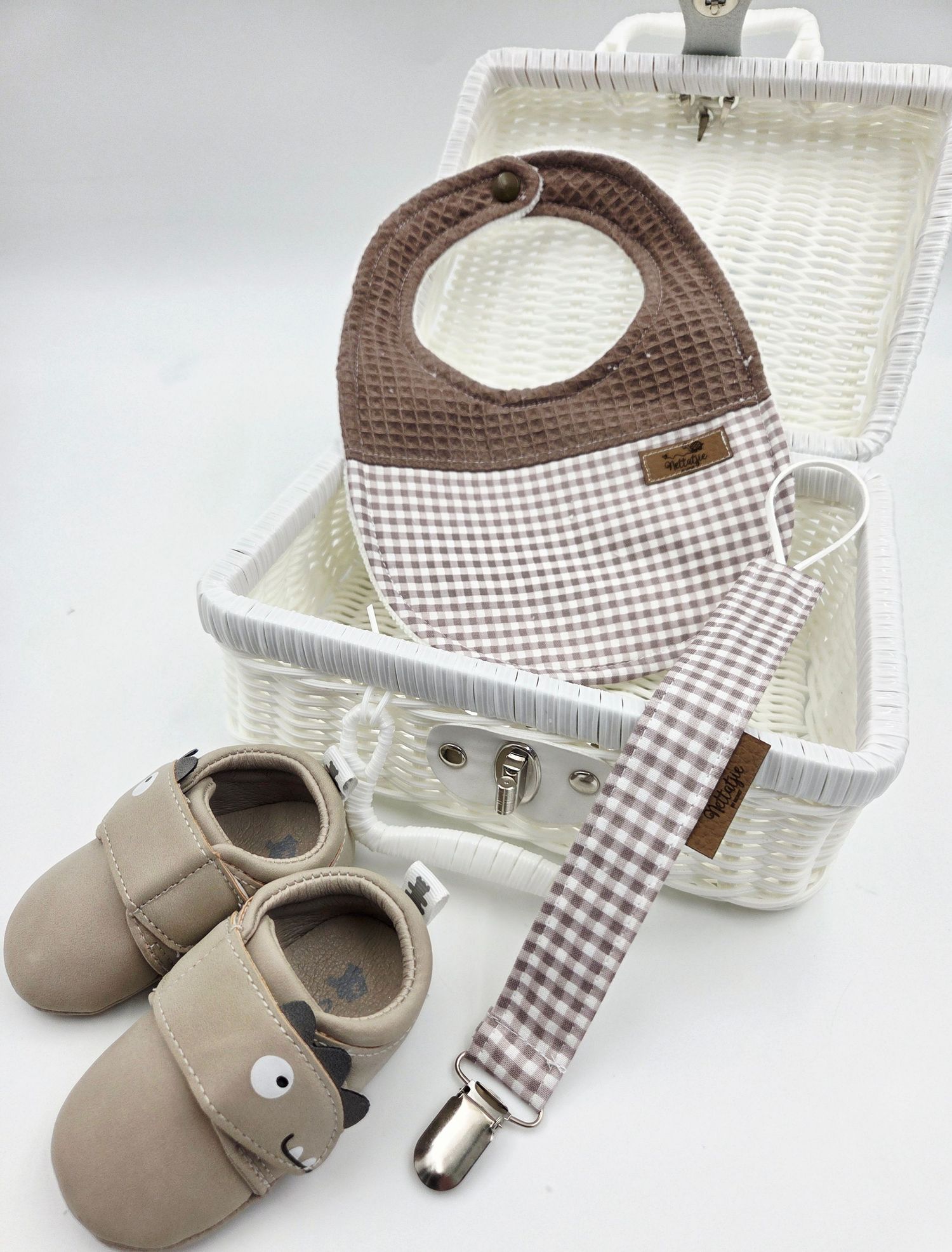 Brown gingham baby bib and shoes set displayed on white wicker basket.