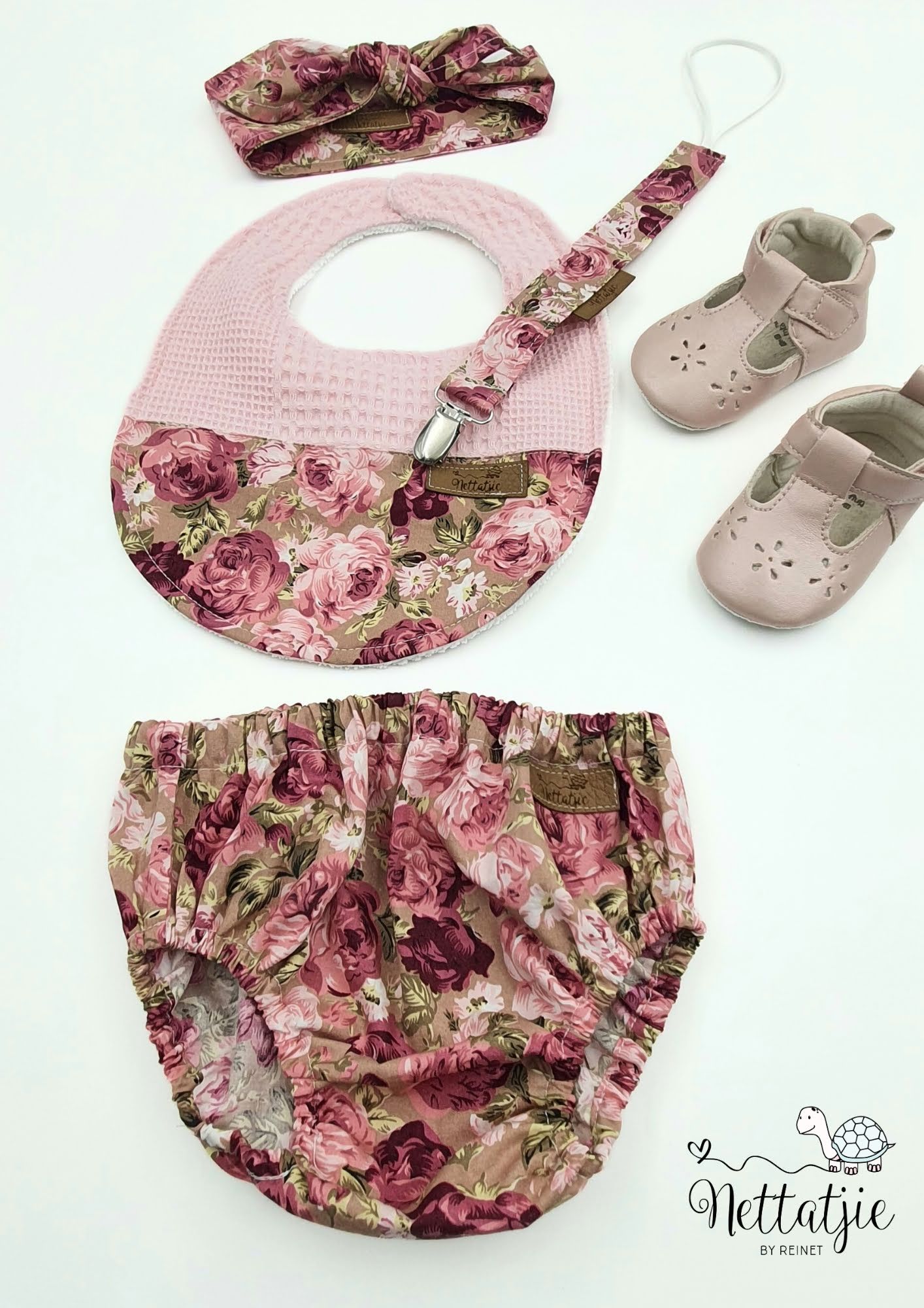 Pink floral baby bloomers and matching accessories laid out on white surface.