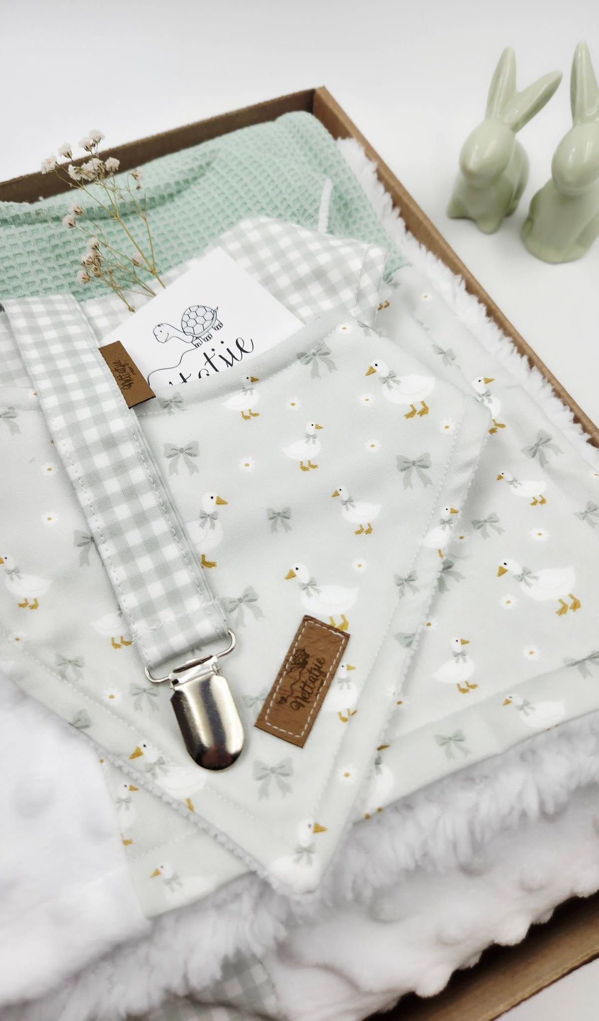 Soft mint baby gift set with gingham pacifier clip, bunny print muslin, fluffy blanket, and ceramic rabbit decor in a wooden box.