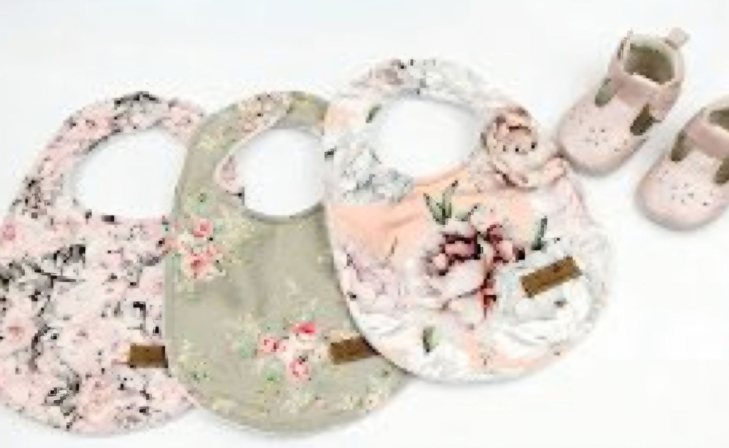 Set of vintage floral baby bibs and matching shoes in soft pink and sage green tones.