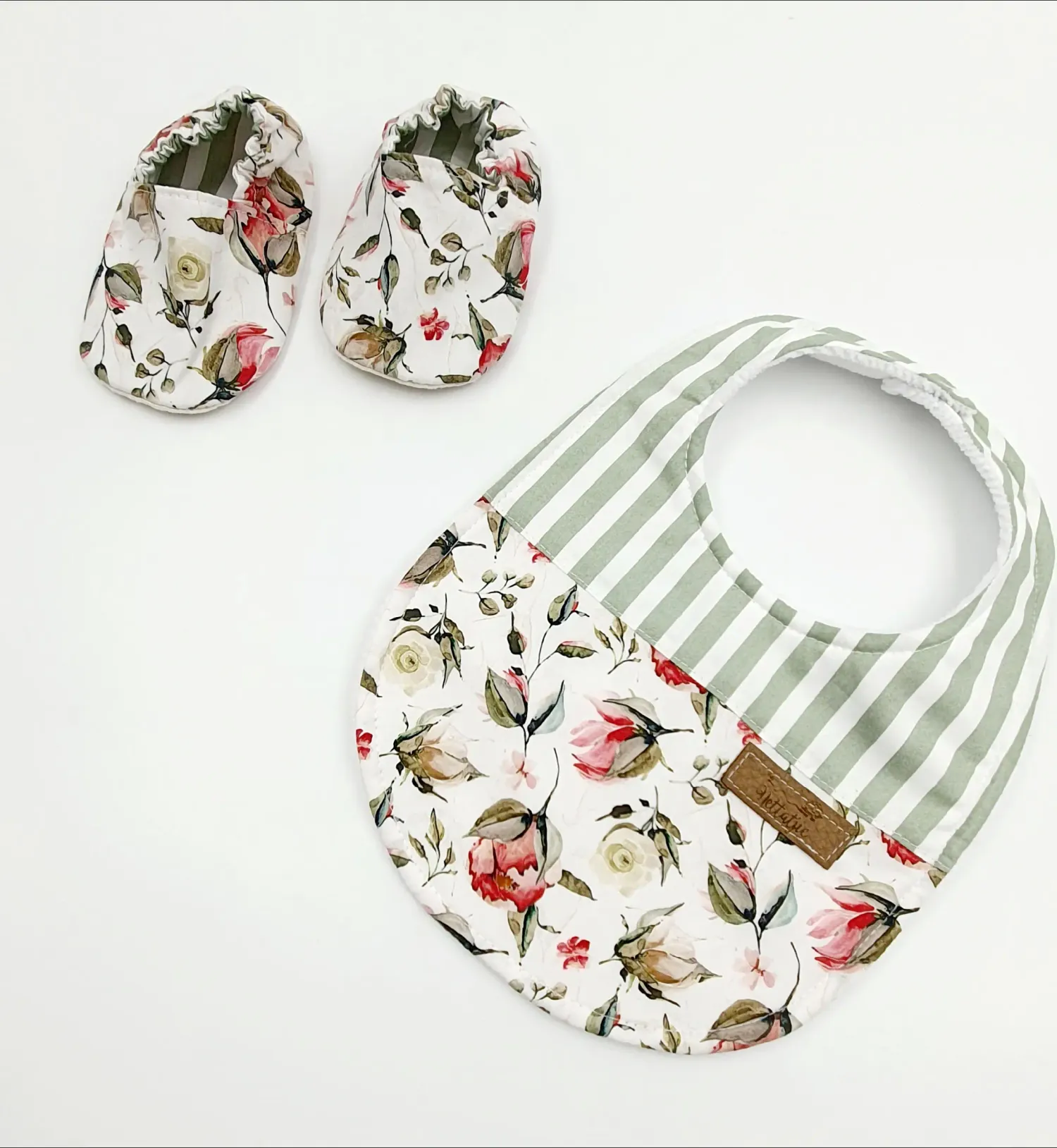 Floral print baby booties and matching bib with gray striped accent and leather tag detail.