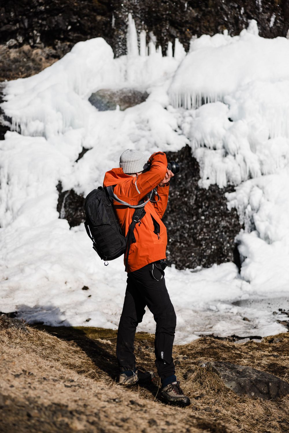Photographer in bright orange jacket shooting against an icy winter backdrop.
