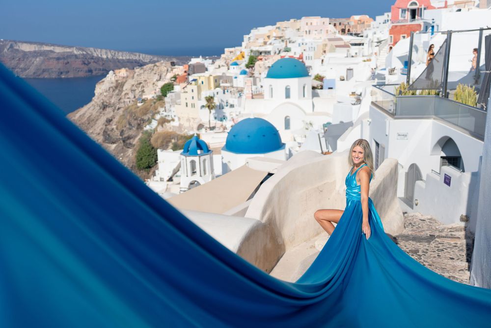 Blue flowing gown contrasts with whitewashed architecture and blue domes in Santorini.