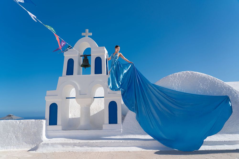 Floating blue fabric creates dramatic scene against white Greek church architecture.