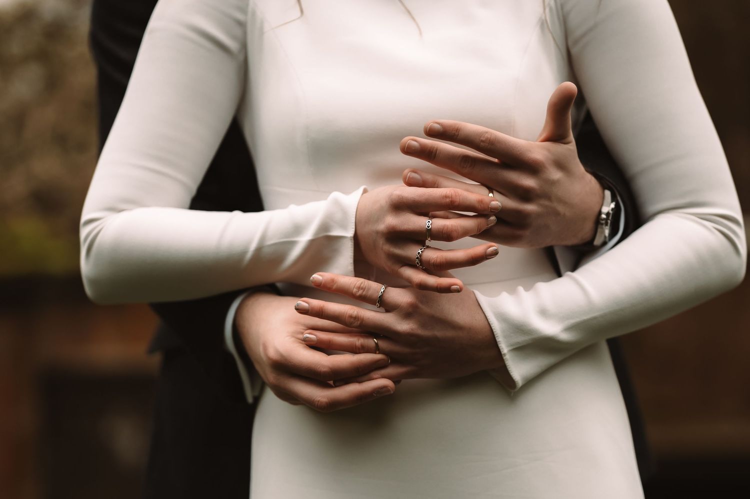 Close-up of hands crossed over a white long-sleeved wedding dress.