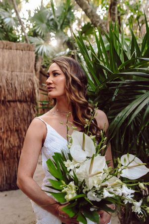 Bride holding a stunning white tropical bouquet with palm leaves in background, Papaya Playa Tulum Wedding.