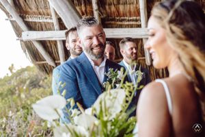 Happy couple shares a loving moment under thatched roof pergola at tropical beach wedding, Papaya Playa Tulum Wedding.