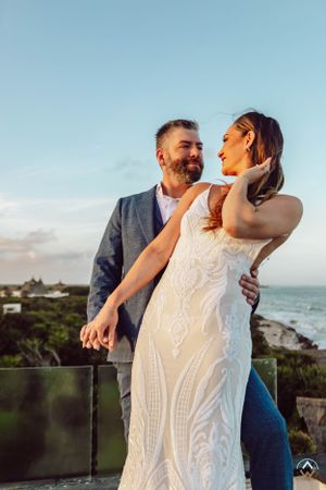 Bride in lace dress and groom in blue suit share romantic moment on oceanfront terrace, Papaya Playa Tulum Wedding.