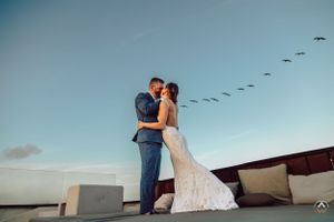 Birds fly overhead as newlyweds embrace on seaside terrace during sunset, Papaya Playa Tulum Wedding.