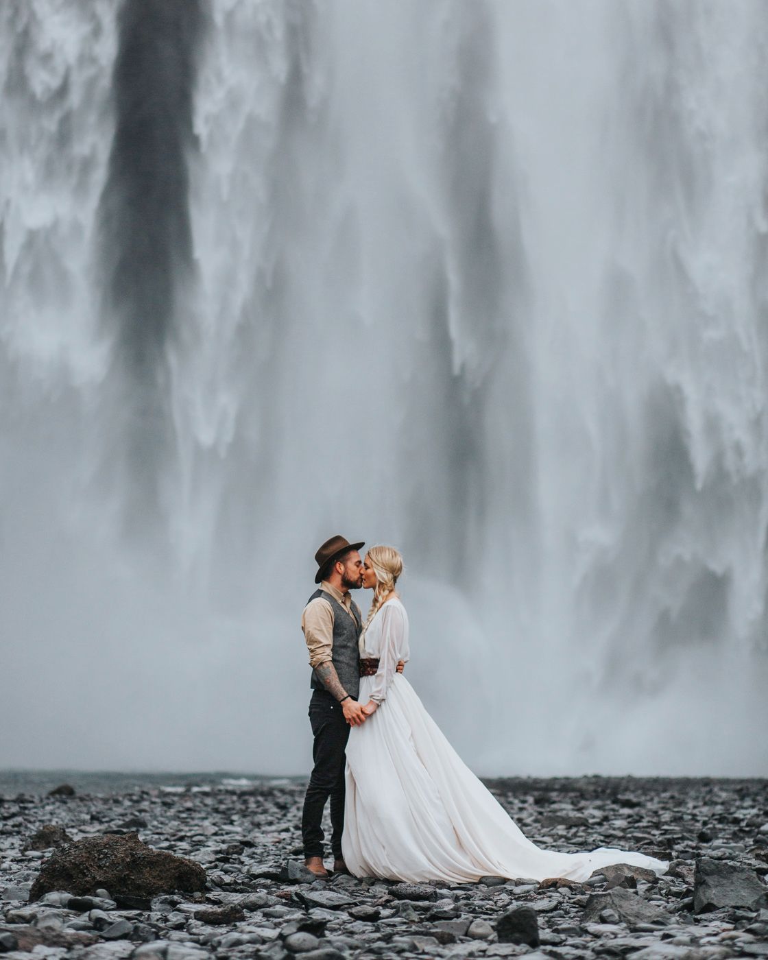 A wedding couple shares a tender moment before a massive misty waterfall.