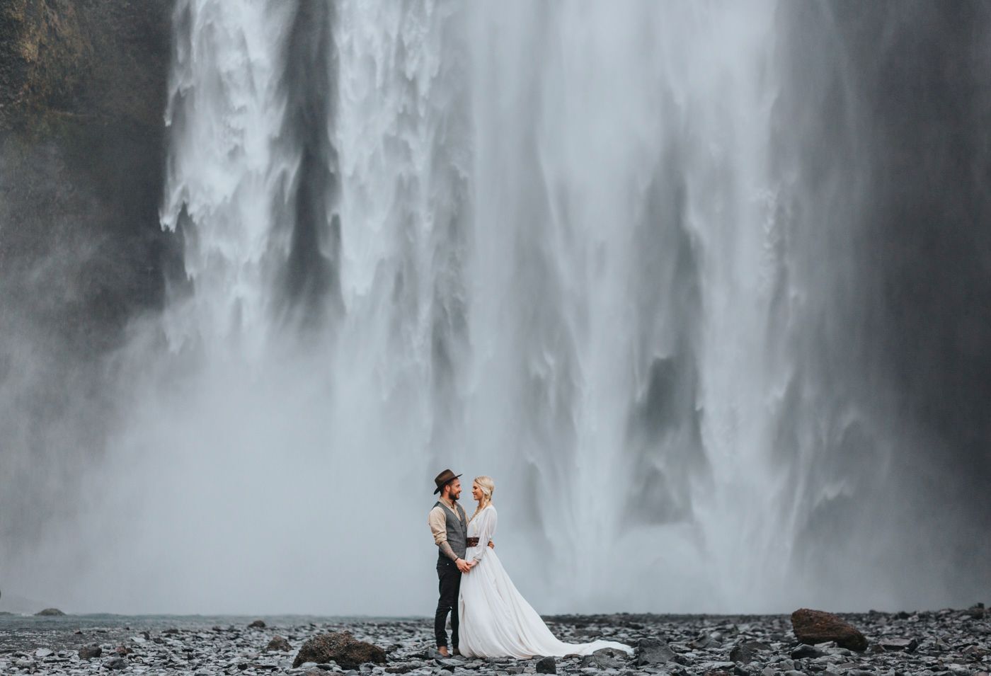 A distant view of newlyweds dwarfed by a magnificent waterfall in Iceland.