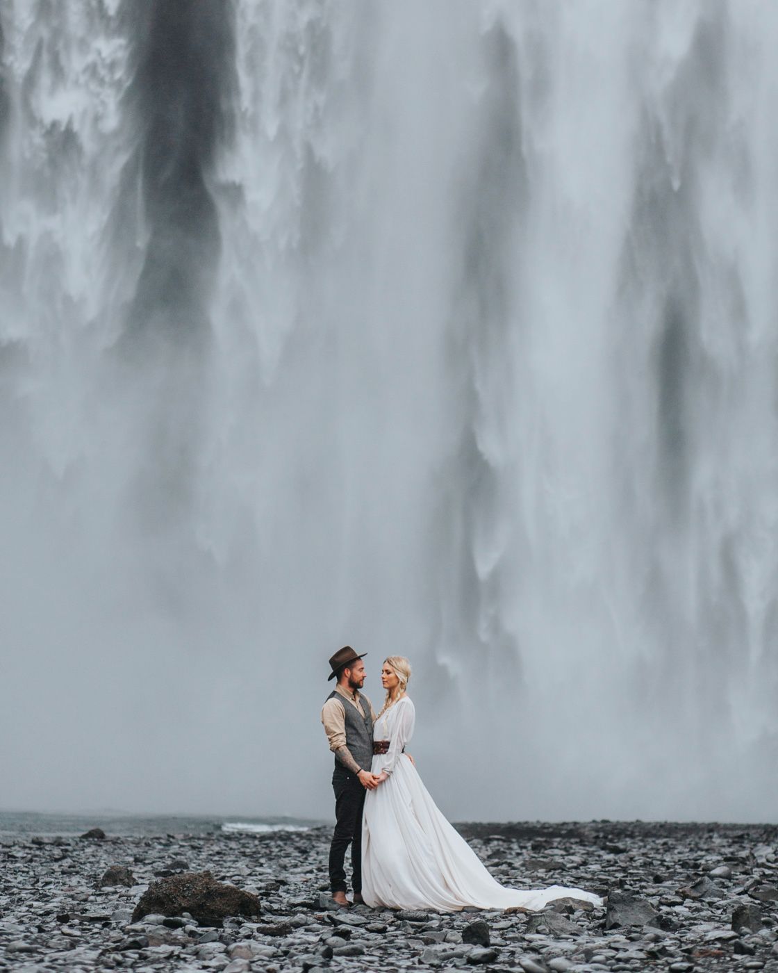 A dreamy wedding portrait with couple standing before the misty Skogafoss waterfall.