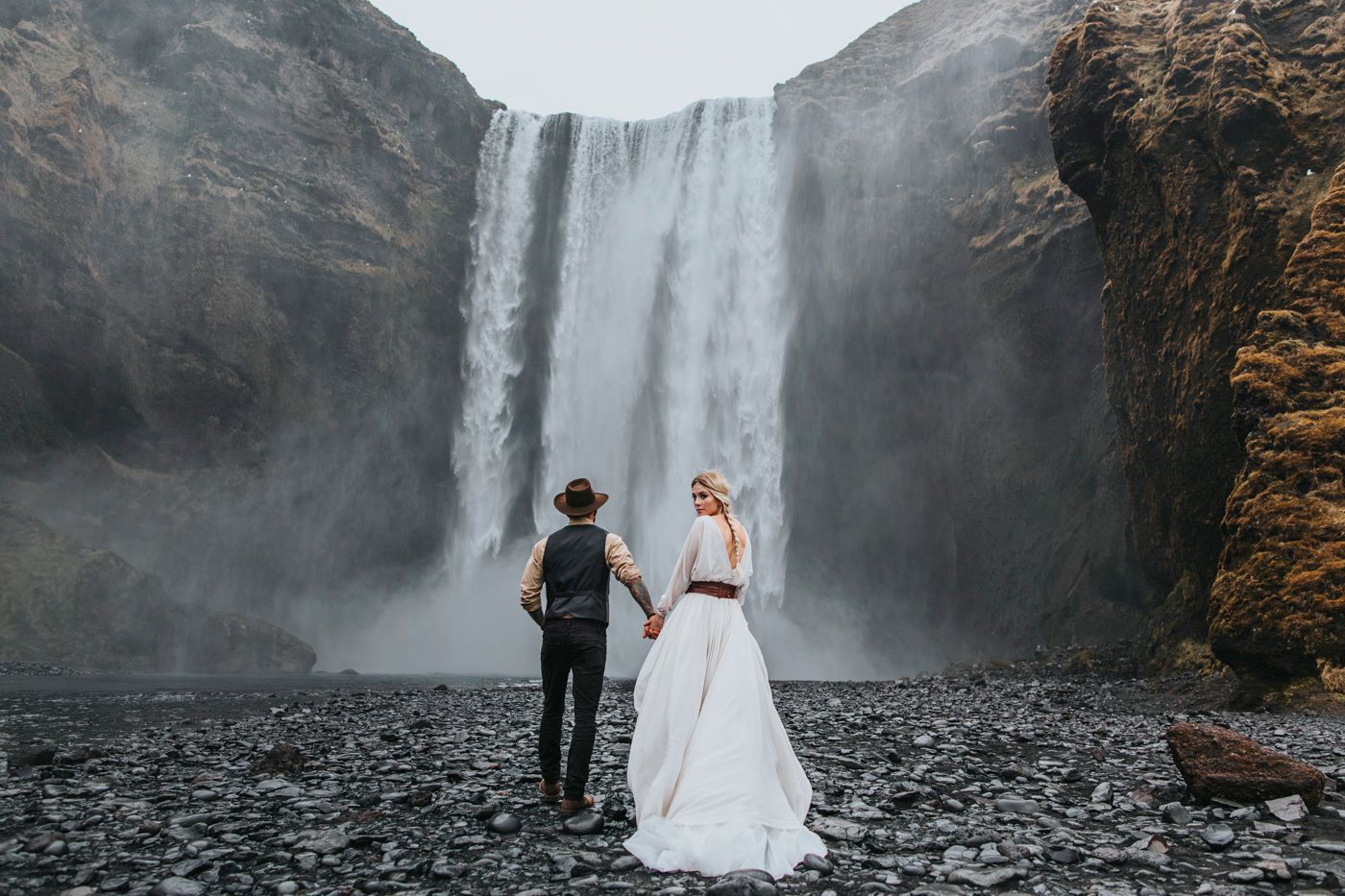A couple in wedding attire viewing a magnificent waterfall in Iceland together.