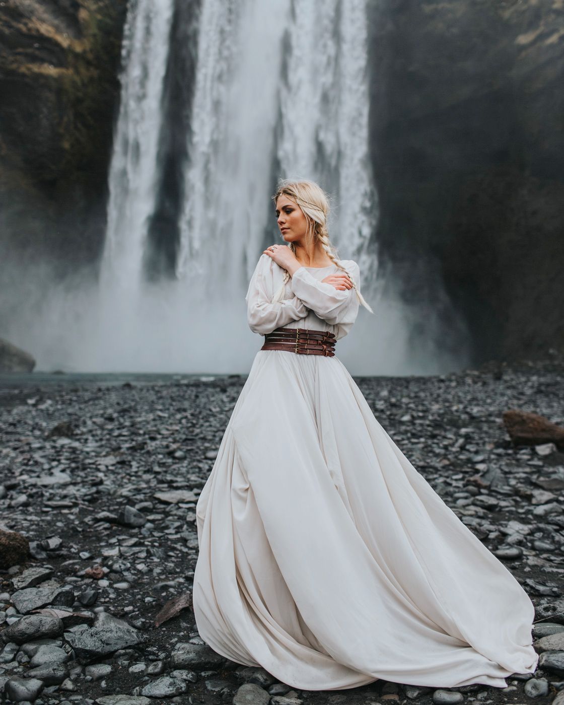 Flowing white wedding dress moves in the wind against dramatic waterfall backdrop.