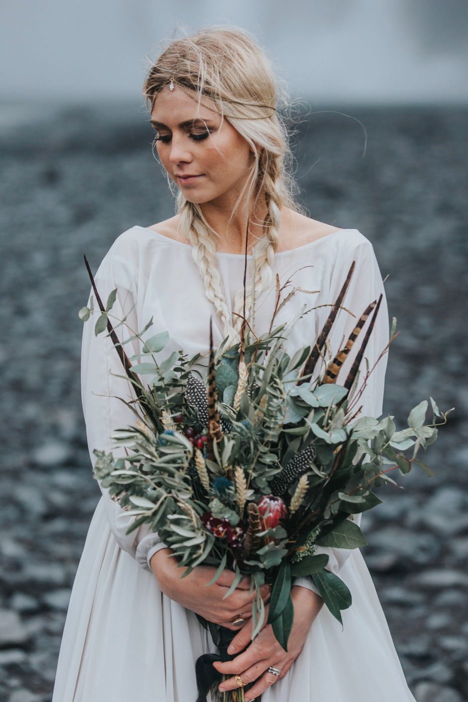 Moody bridal portrait with wild flower bouquet against cascading waterfall backdrop.