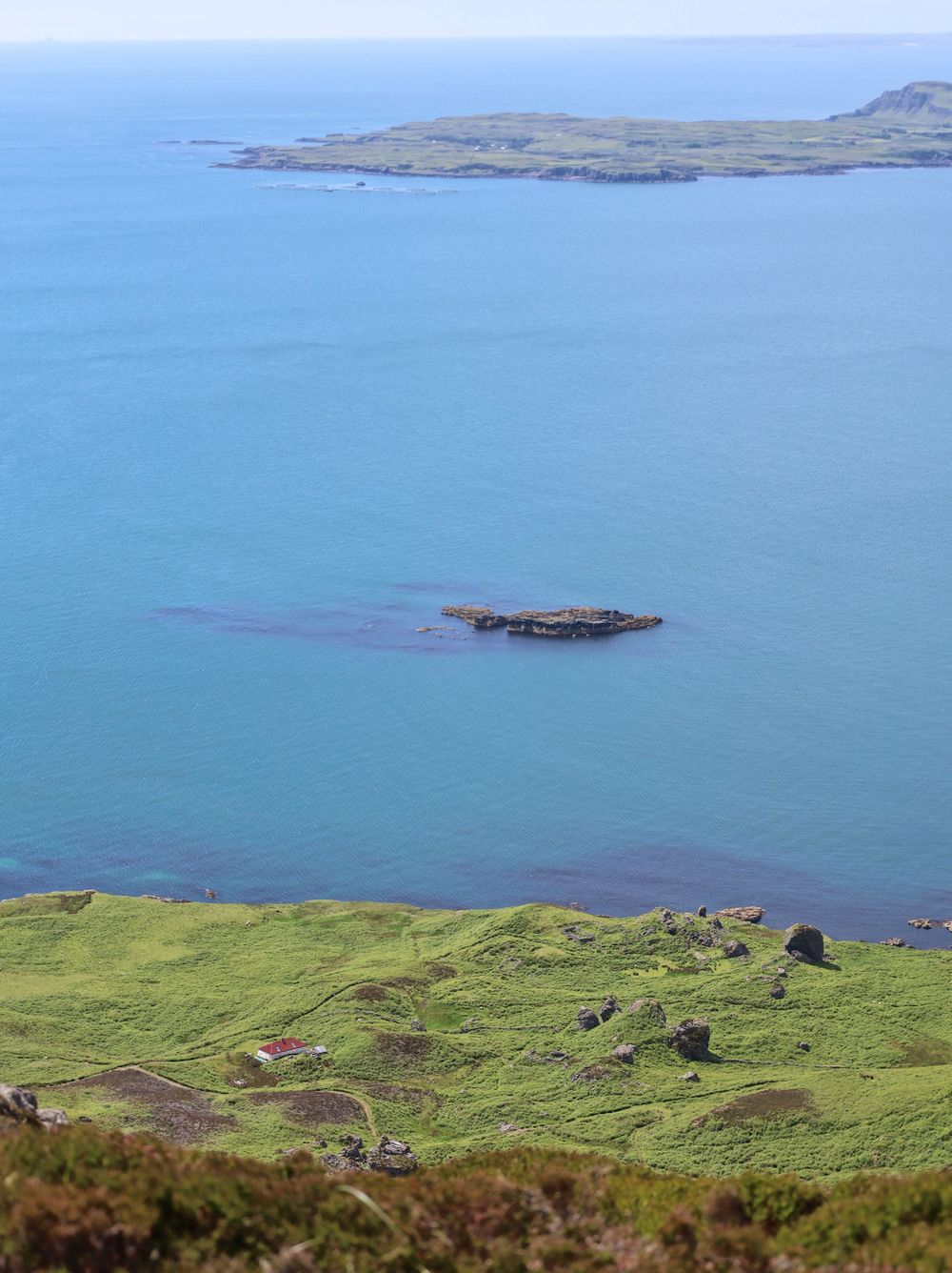 Coastal aerial view showing green cliffs meeting turquoise waters with small islands visible.