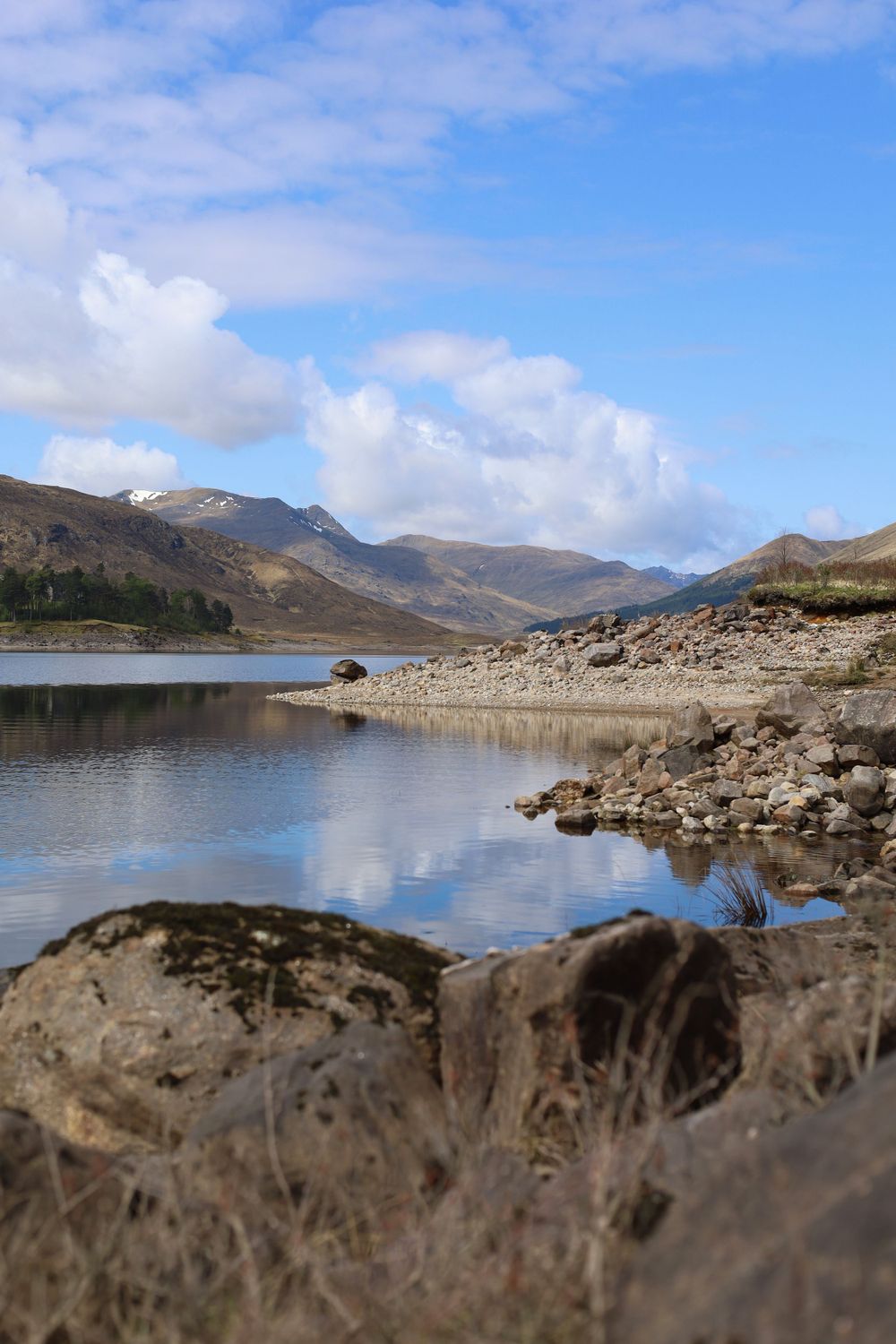 Scenic mountain lake with rocky shore and hills reflecting in clear water.
