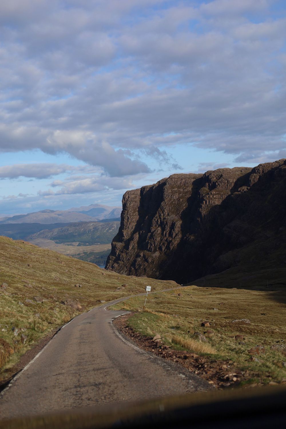 Winding mountain road through dramatic Highland landscape with steep cliffs.