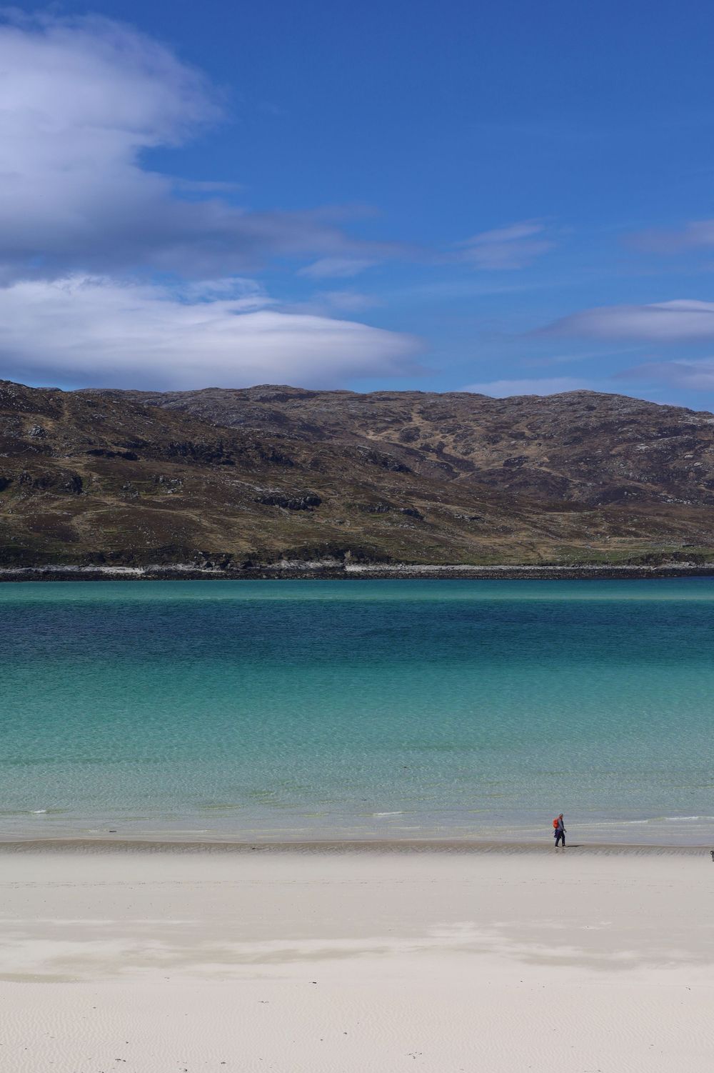 Pristine turquoise bay with white sandy beach and rugged hills in the Scottish Highlands.