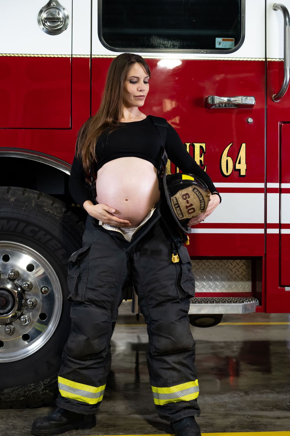 An artistic maternity photo shoot in front of a red fire truck with reflective safety gear.
