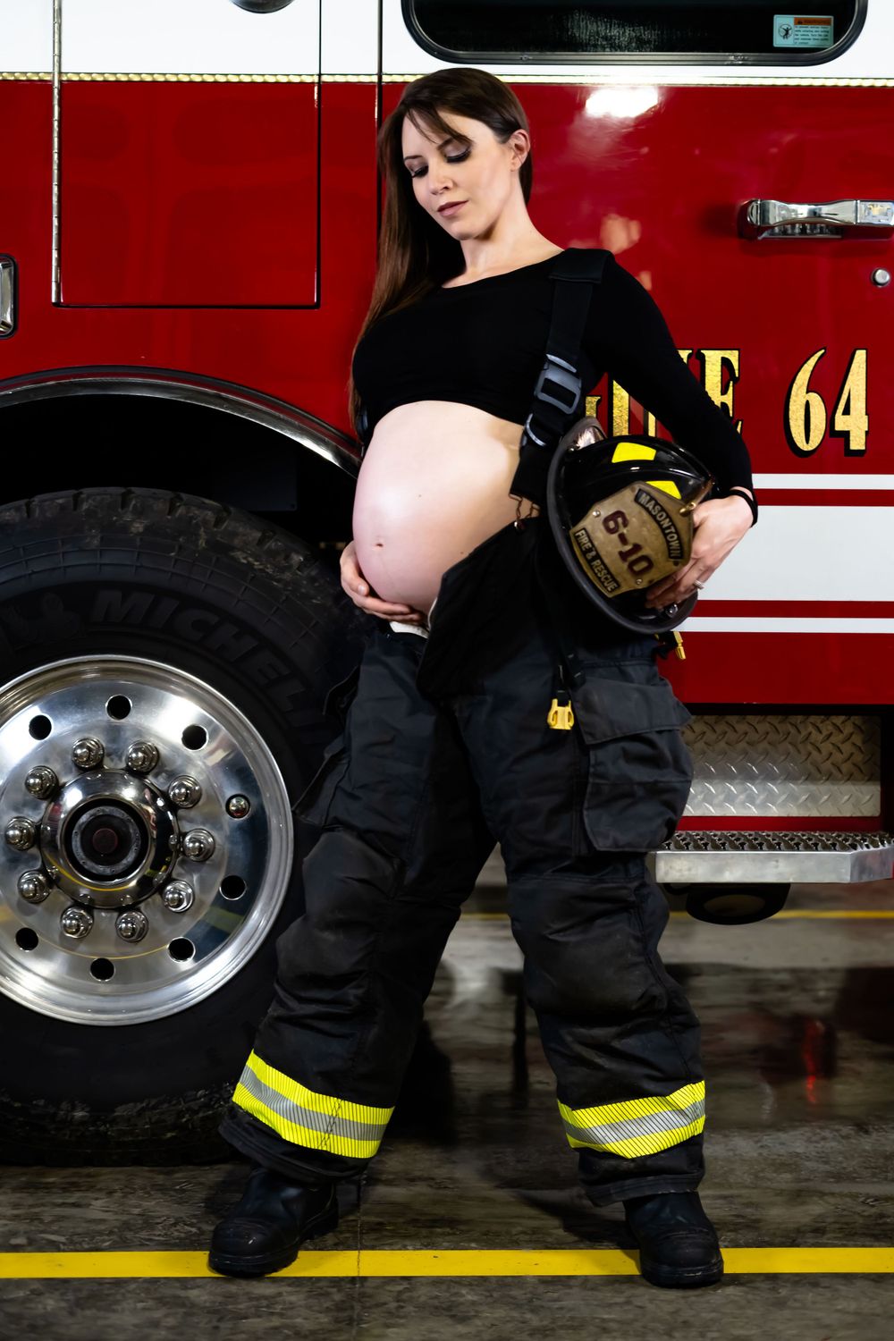 Dramatic maternity photo with fire station equipment and reflective uniform details.