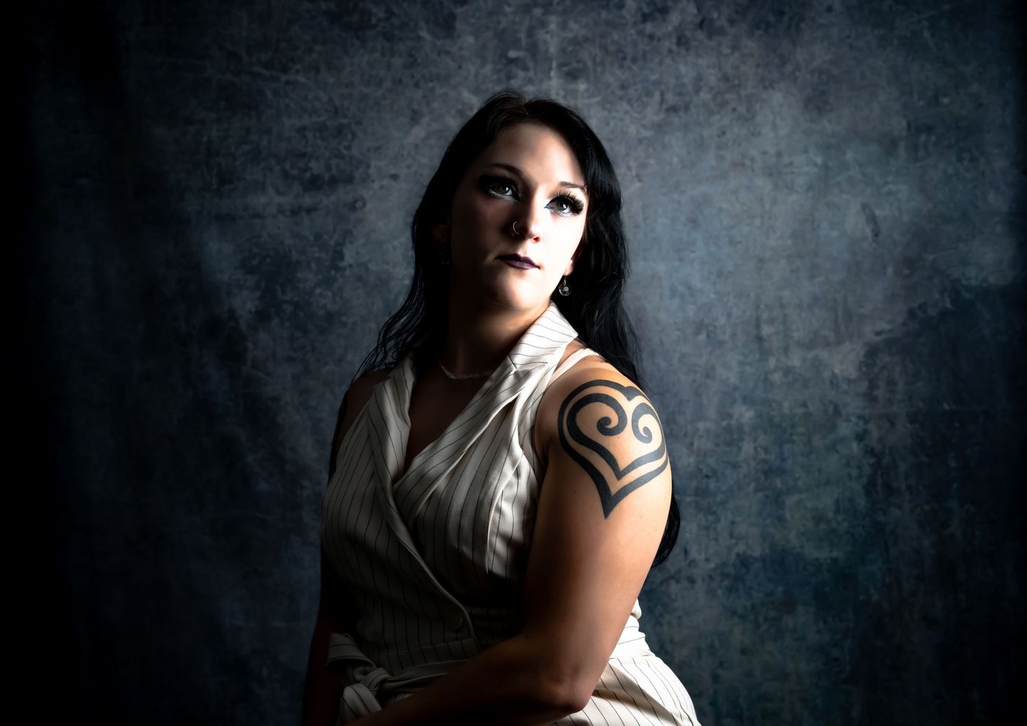 Dramatic portrait against textured grey background showing a tribal arm tattoo.