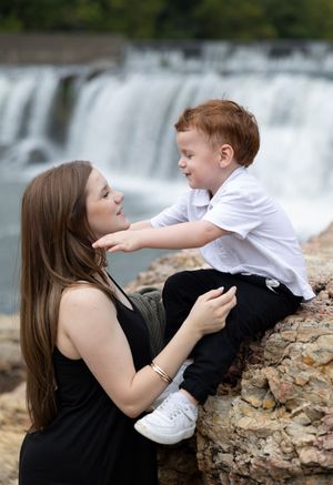Playful interaction between parent and child on rocky ledge with waterfall backdrop.