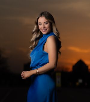 Maternity photoshoot at sunset featuring a person in a royal blue dress against a dramatic orange sky.