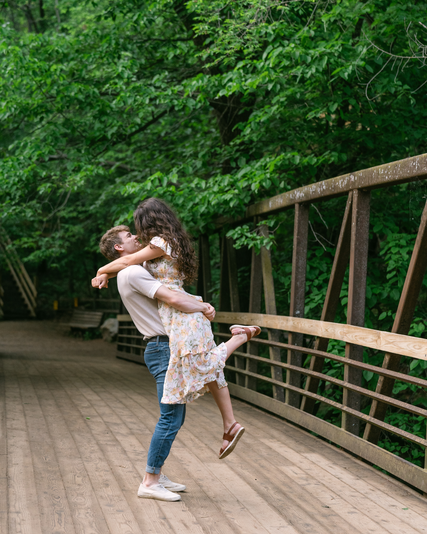 Playful kiss as he lifts her on the bridge during a golden hour engagement session at Willow River