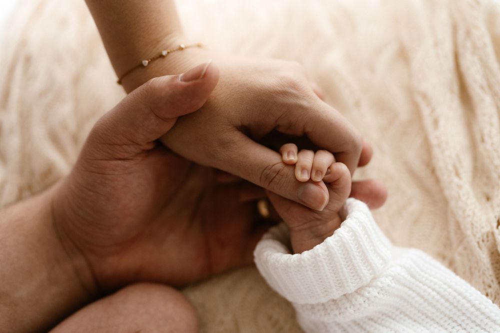 Two adult hands gently cradling a newborn baby's tiny hand, symbolizing love and family connection.