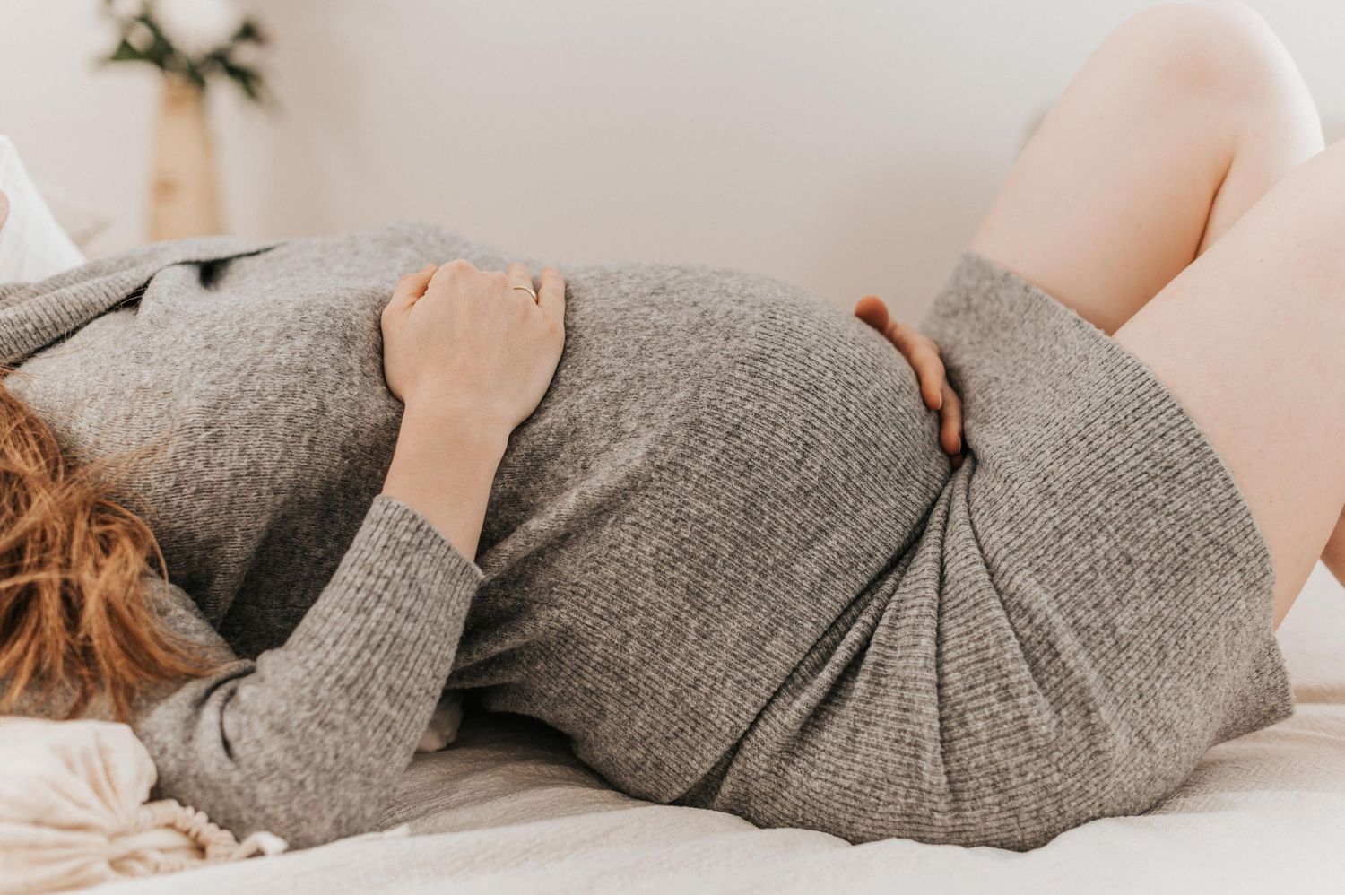 Side view of a pregnant person resting on gray bedding in comfortable clothing.
