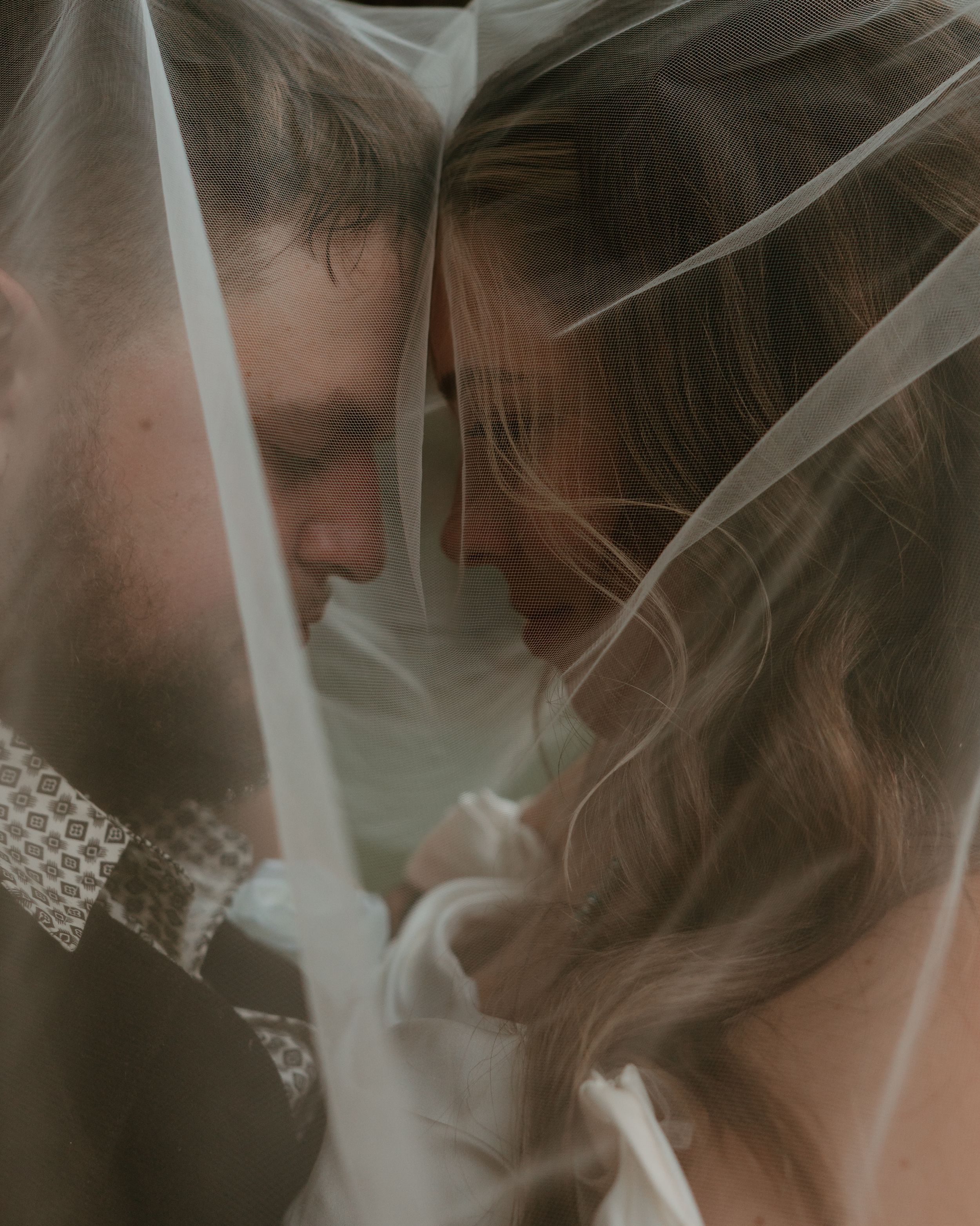 Romantic couple embracing under sheer white veil in soft moody lighting creating an intimate atmosphere.