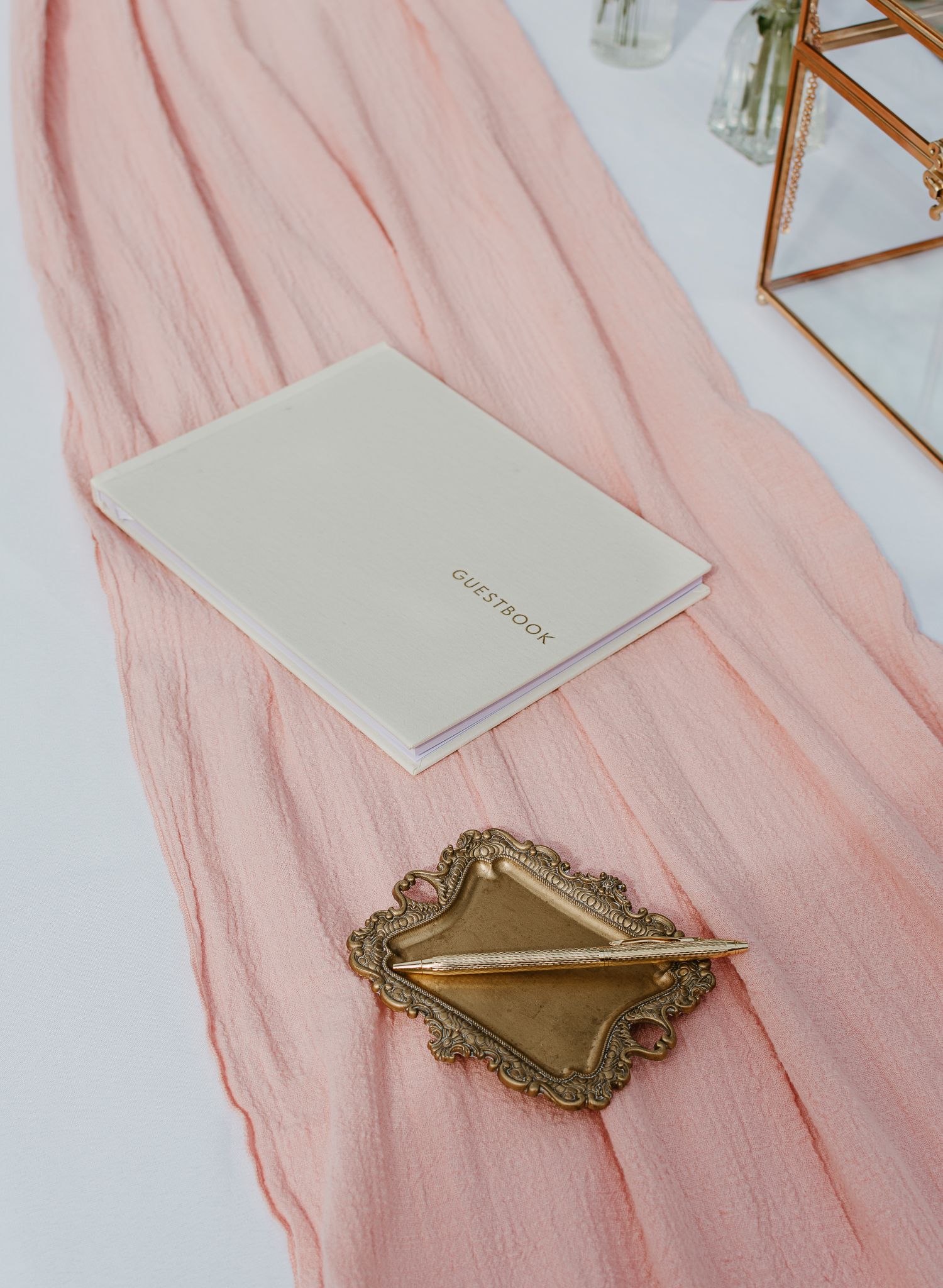 Pink fabric runner with vintage gold frames and white stationery on display.
