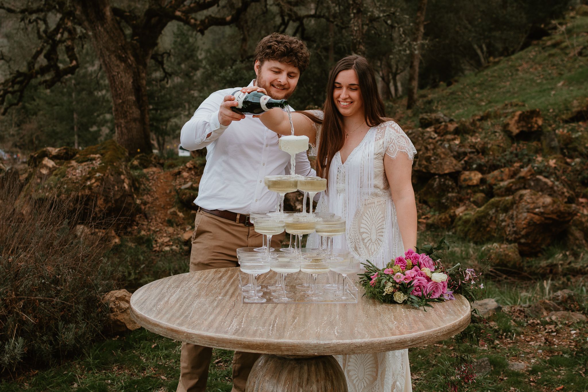 Romantic outdoor engagement session with vintage decor and champagne glasses on rustic table.