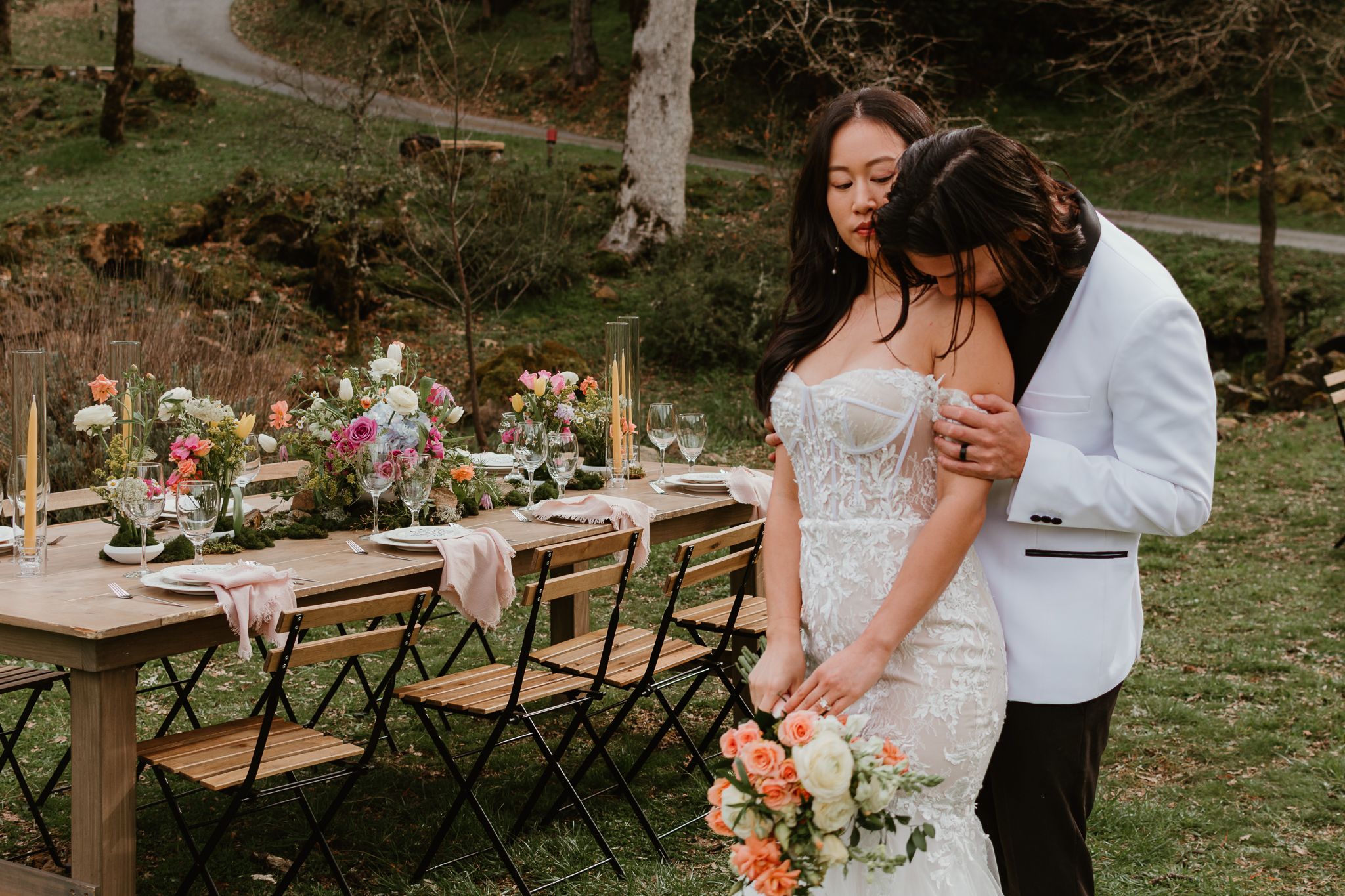 A romantic outdoor wedding scene with a couple embracing near rustic wooden benches and floral decorations.