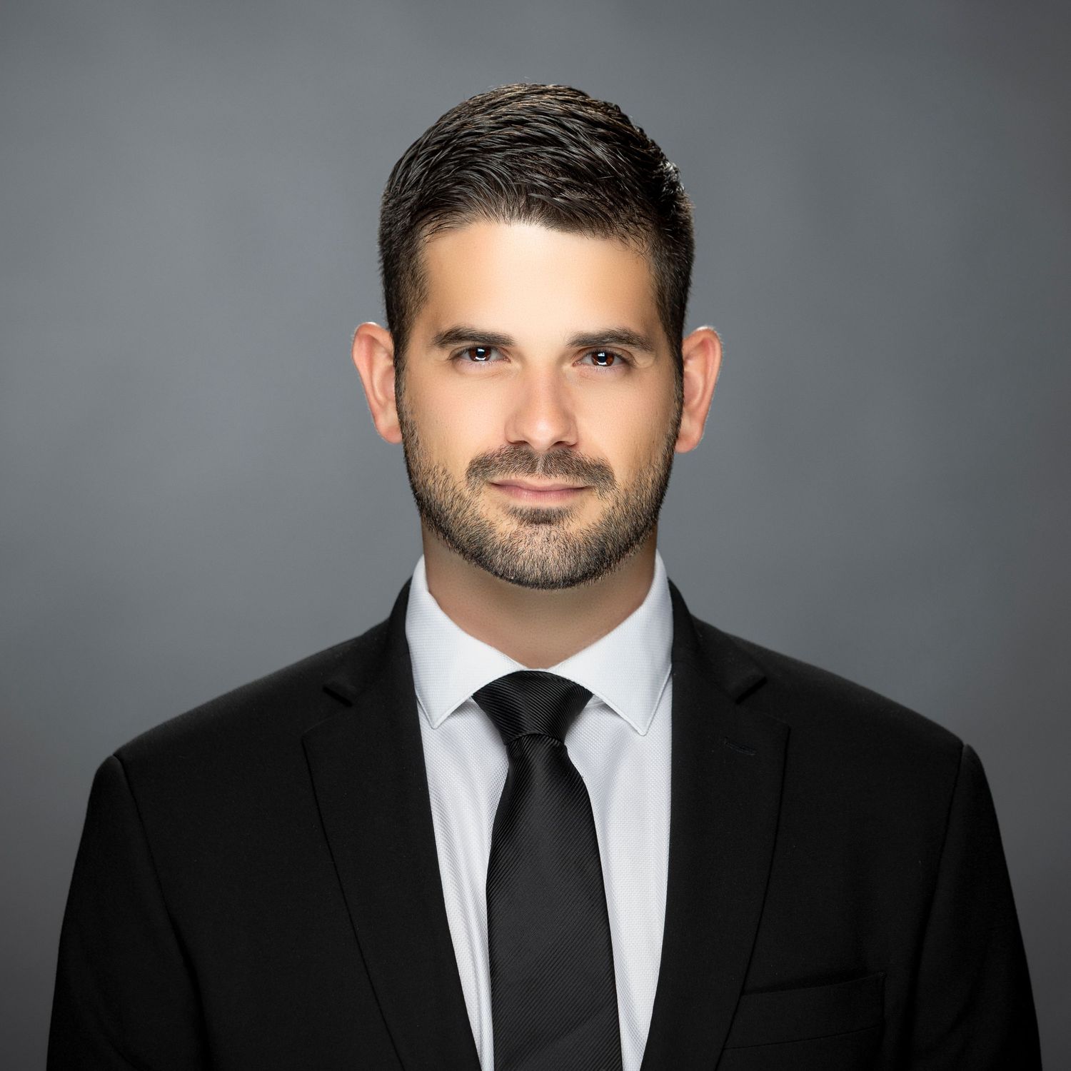 Professional headshot portrait of a person in a black suit and tie against a gray background.