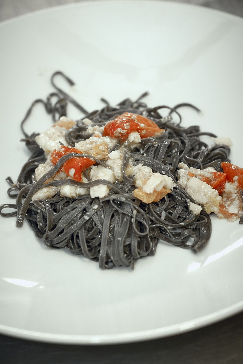 Black squid ink pasta with seafood and red sauce garnish served on a white plate.