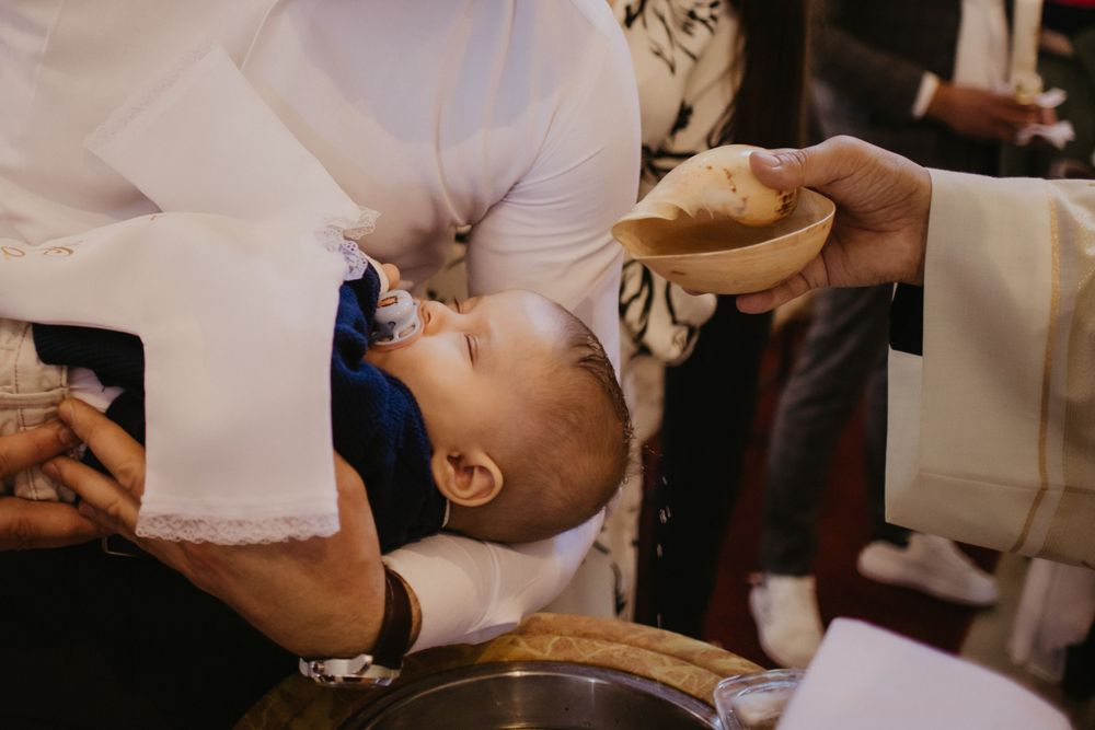 A baby receiving baptism with holy water during a traditional church ceremony.