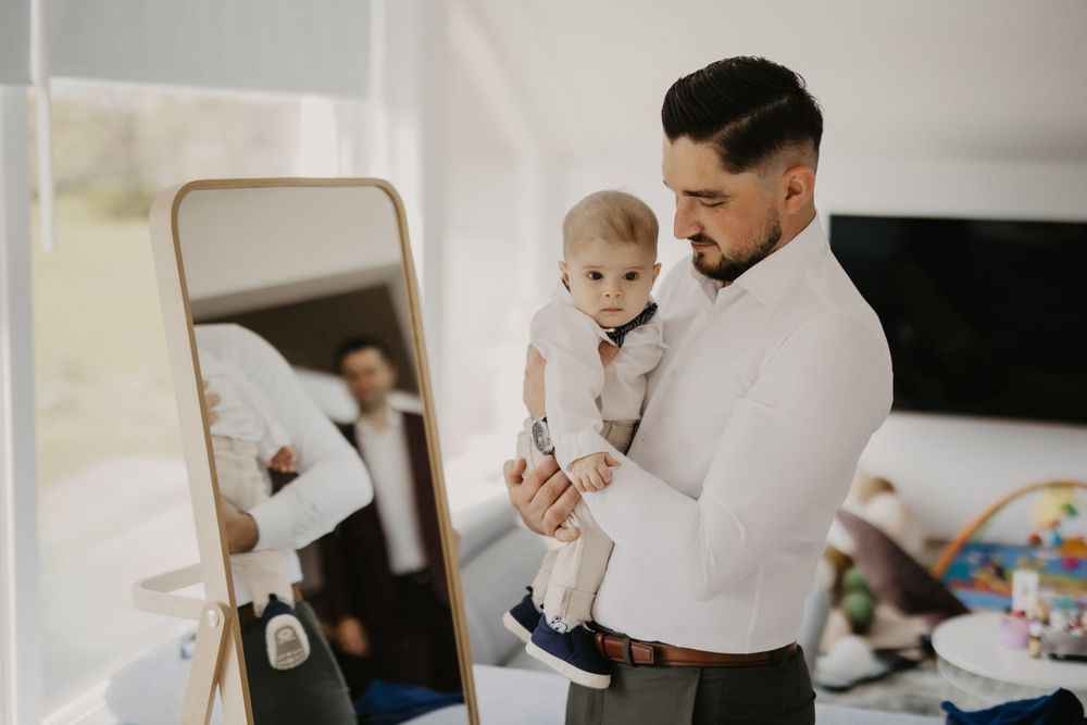 Family moment captured in mirror reflection showing dressed up adults and baby.