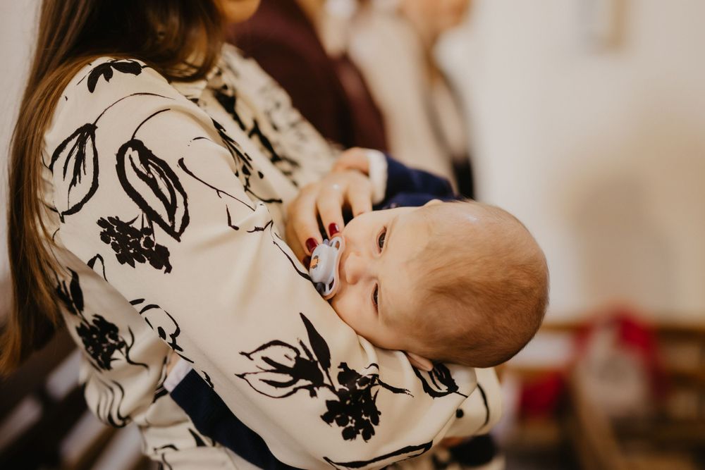 Baby in floral print clothing sleeps peacefully during baptism ceremony.