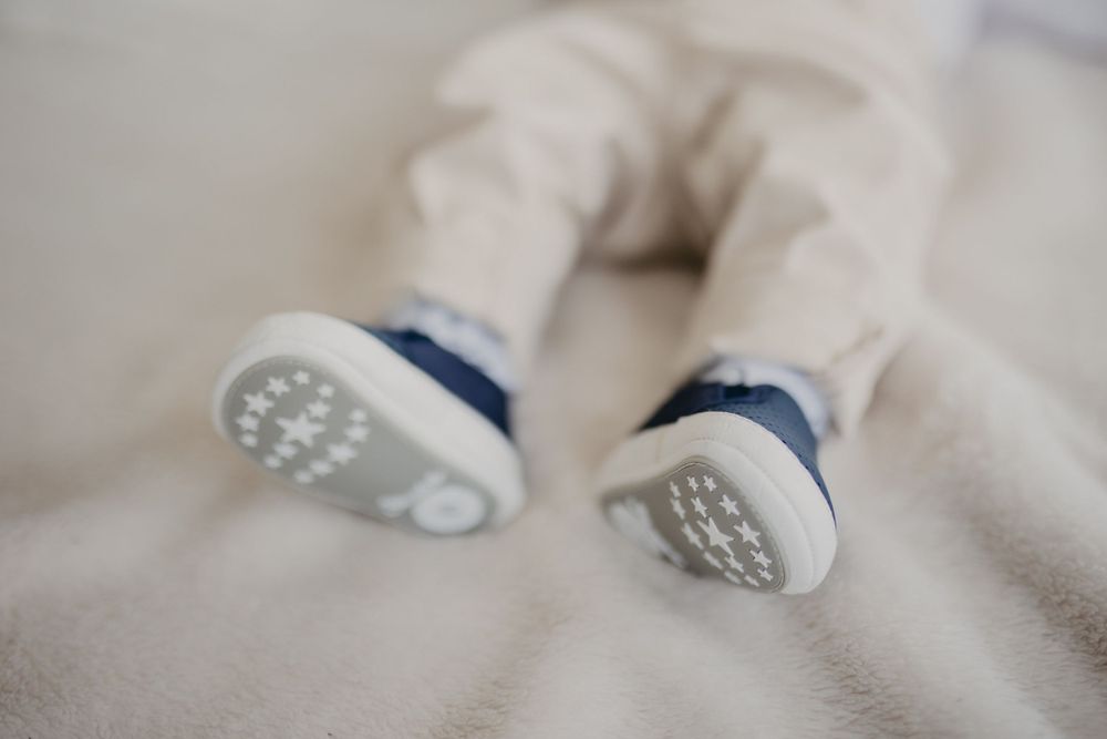 Close up of baby shoes with white soles and blue trim on light surface.