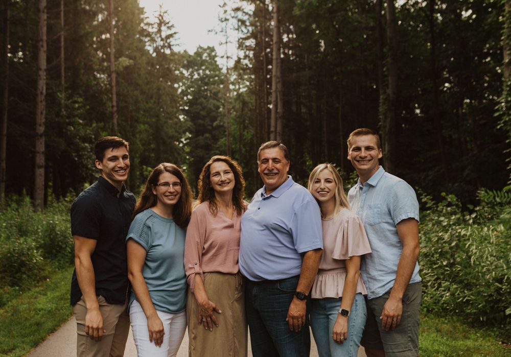 A family group of six people stands together on a paved forest trail.