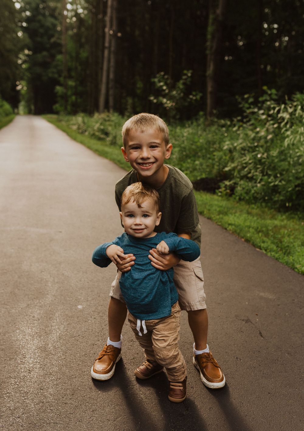 Two young children play together on a paved forest path during a photo session.